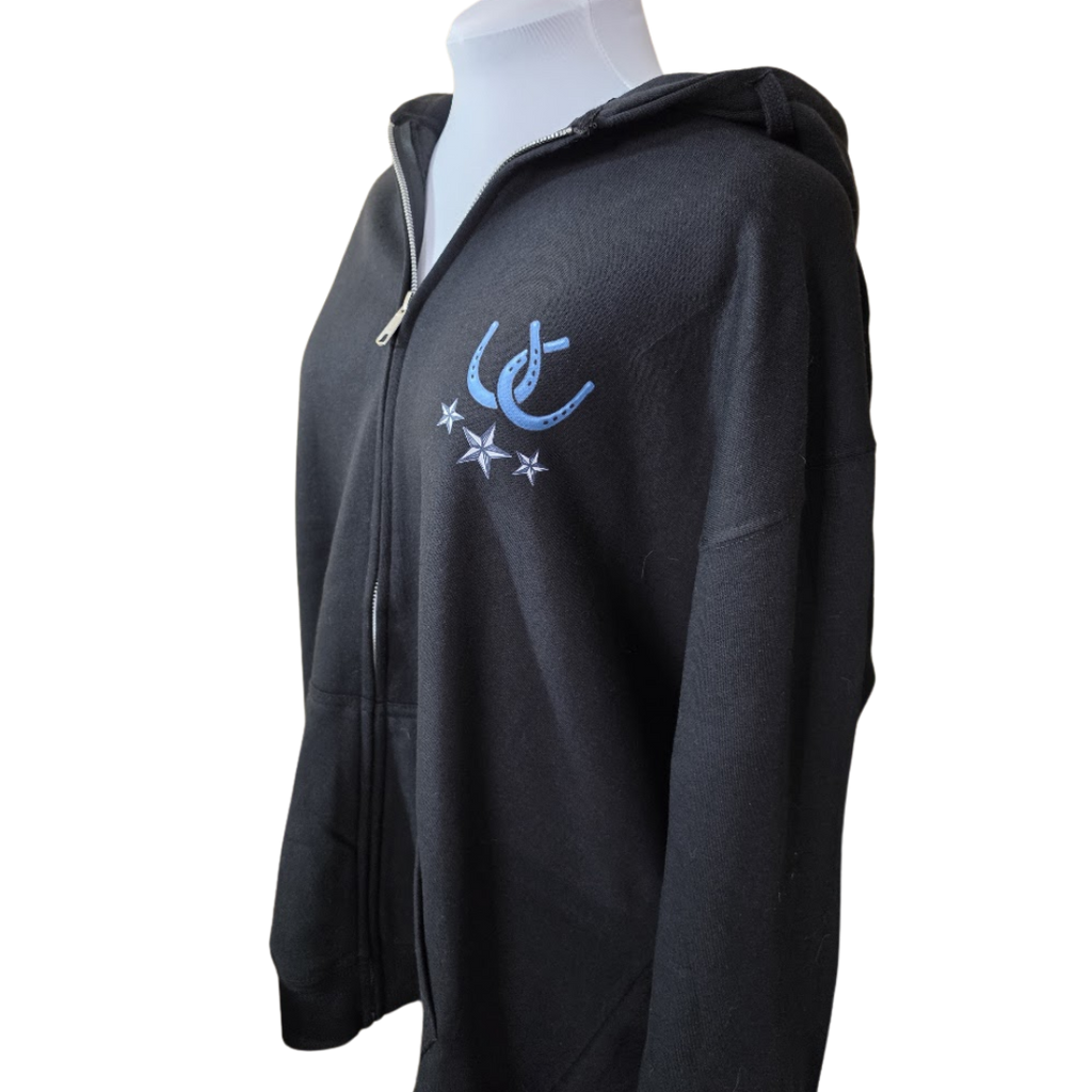 A black zip-up hoodie displayed on a white mannequin torso against a plain white background. The hoodie features a light blue  horseshoe and stars logo on the left chest.