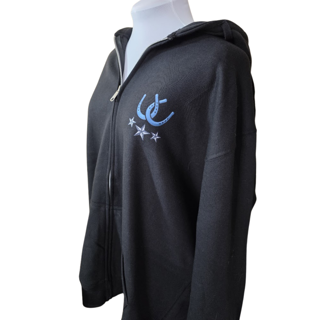 A black zip-up hoodie displayed on a white mannequin torso against a plain white background. The hoodie features a light blue  horseshoe and stars logo on the left chest.