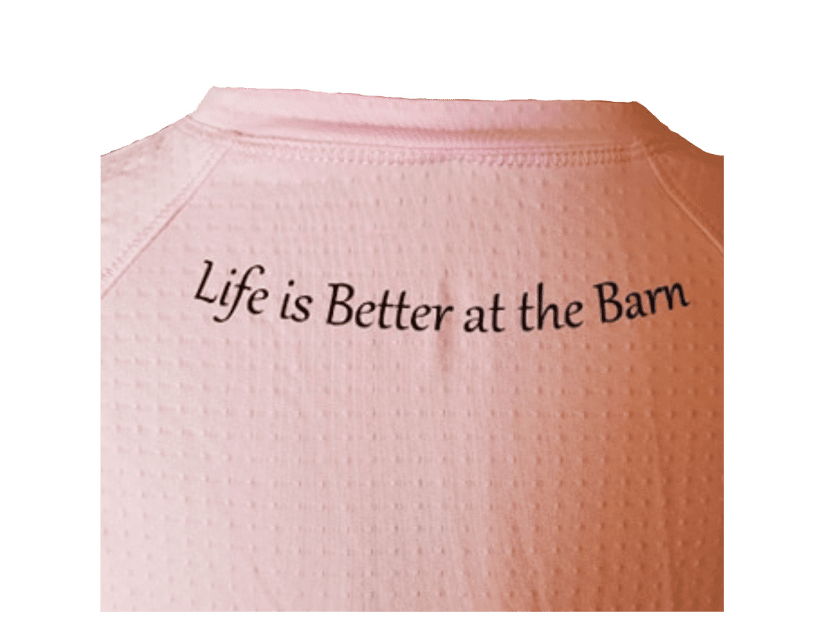 A close-up of a light pink textured t-shirt with the phrase 'Life is Better at the Barn' printed in black script across the chest.