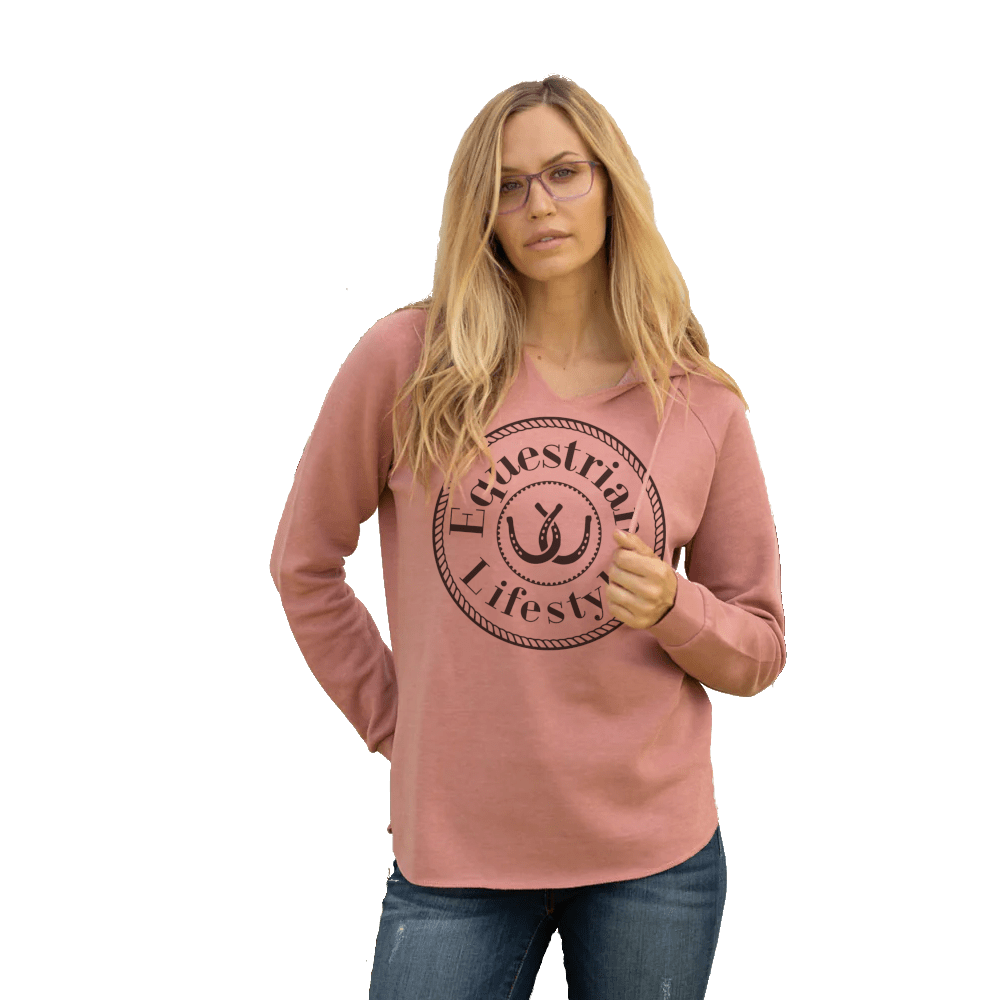 A woman with blonde hair and glasses wearing a dusty rose long-sleeve shirt with a dark brown circular graphic that reads 'Equestrian Lifestyle' with an horseshoe symbol, paired with blue jeans, set against a plain white background.