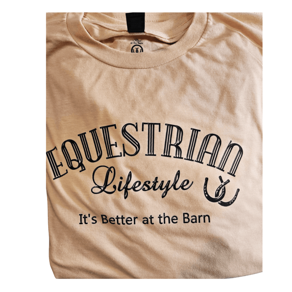A beige t-shirt with a black graphic print that reads 'EQUESTRIAN Lifestyle It's Better at the Barn' along with a horseshoe illustration, shown on a plain white background.