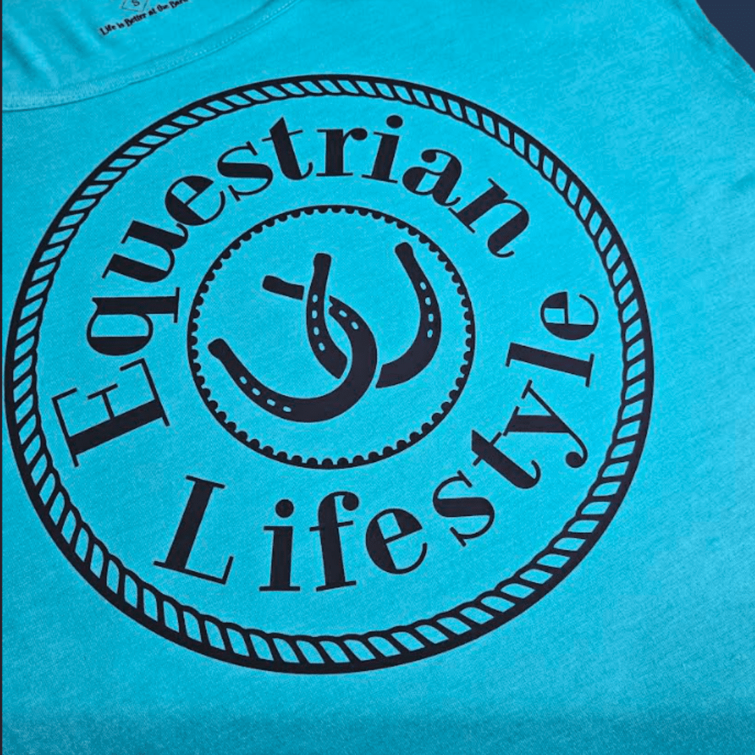 A close-up of a bright turquoise blue t-shirt featuring a large black circular graphic with the words 'Equestrian Lifestyle' and a stylized horseshoe logo in the center.