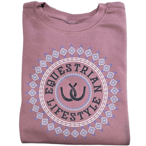 A folded dusty rose t-shirt featuring a circular graphic with the words 'EQUESTRIAN LIFESTYLE' in black, flanked by two black horseshoes, all enclosed in a white and light blue geometric aztec pattern.