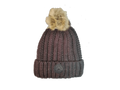A ribbed knit beanie hat in a dark plum-brown color with a fluffy beige faux-fur pom-pom on top and a circular leatherette equestrian lifestyle  brand patch on the front cuff.